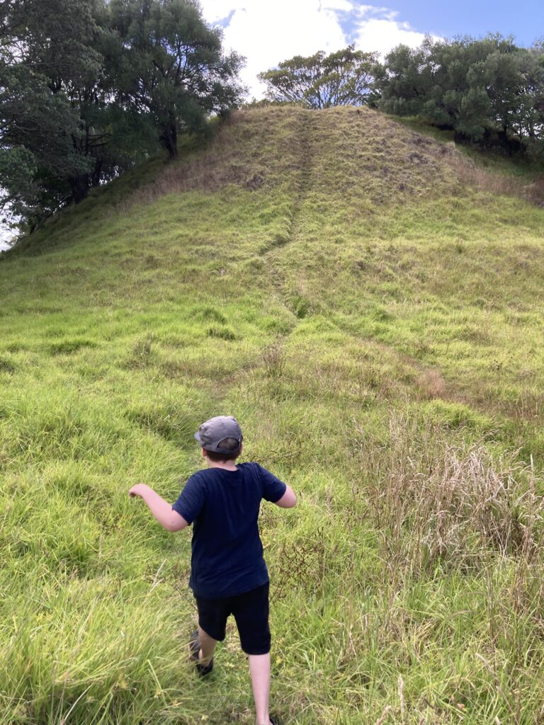 A small picture of one of the volcanic cones, with a path worn into the grass. A small boy is approaching the path.