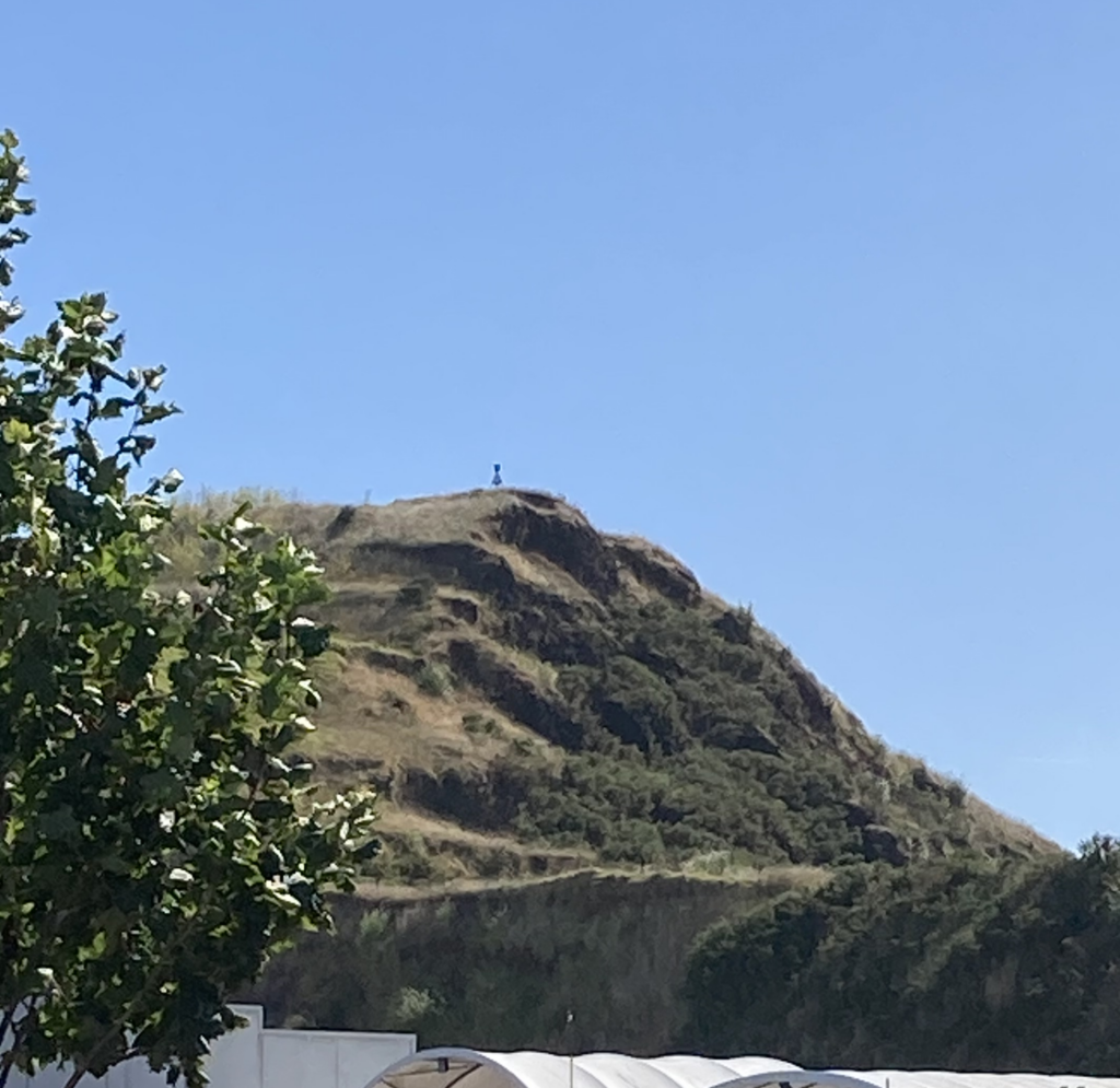 A grainy, zoomed-in picture of  a steep pyramid shaped volcano. A trig station is just visible on the summit.